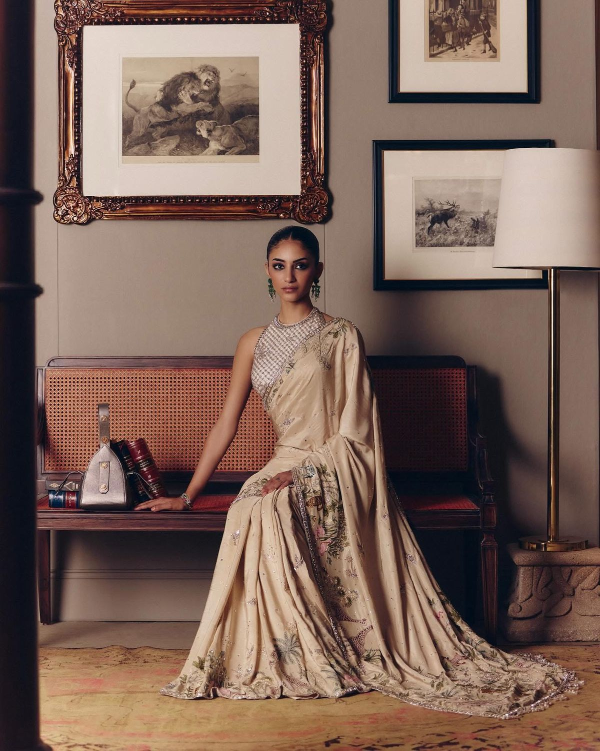 A woman seated in a cream silk saree with floral embroidery, in a warm panelled interior